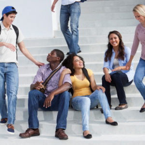 Multi-ethnic teenage students on steps of school building.